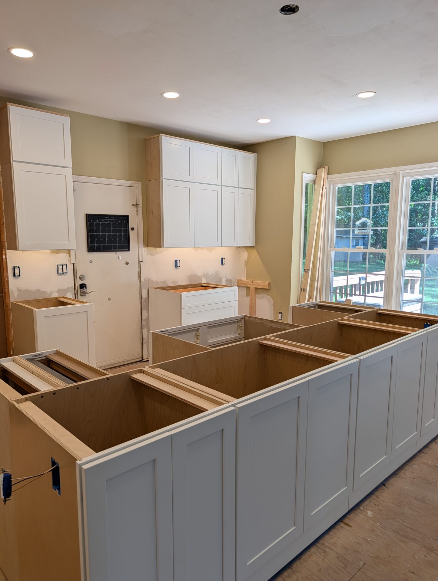 Kitchen remodel in progress with white shaker upper cabinets installed and grey island framed on the subfloor