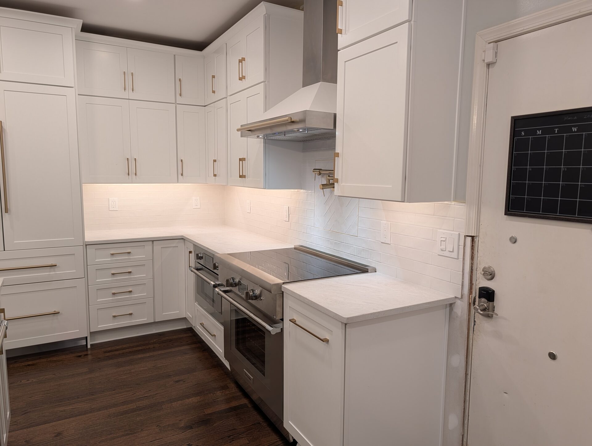 Finished range wall with stainless chimney hood and white herringbone tile backsplash