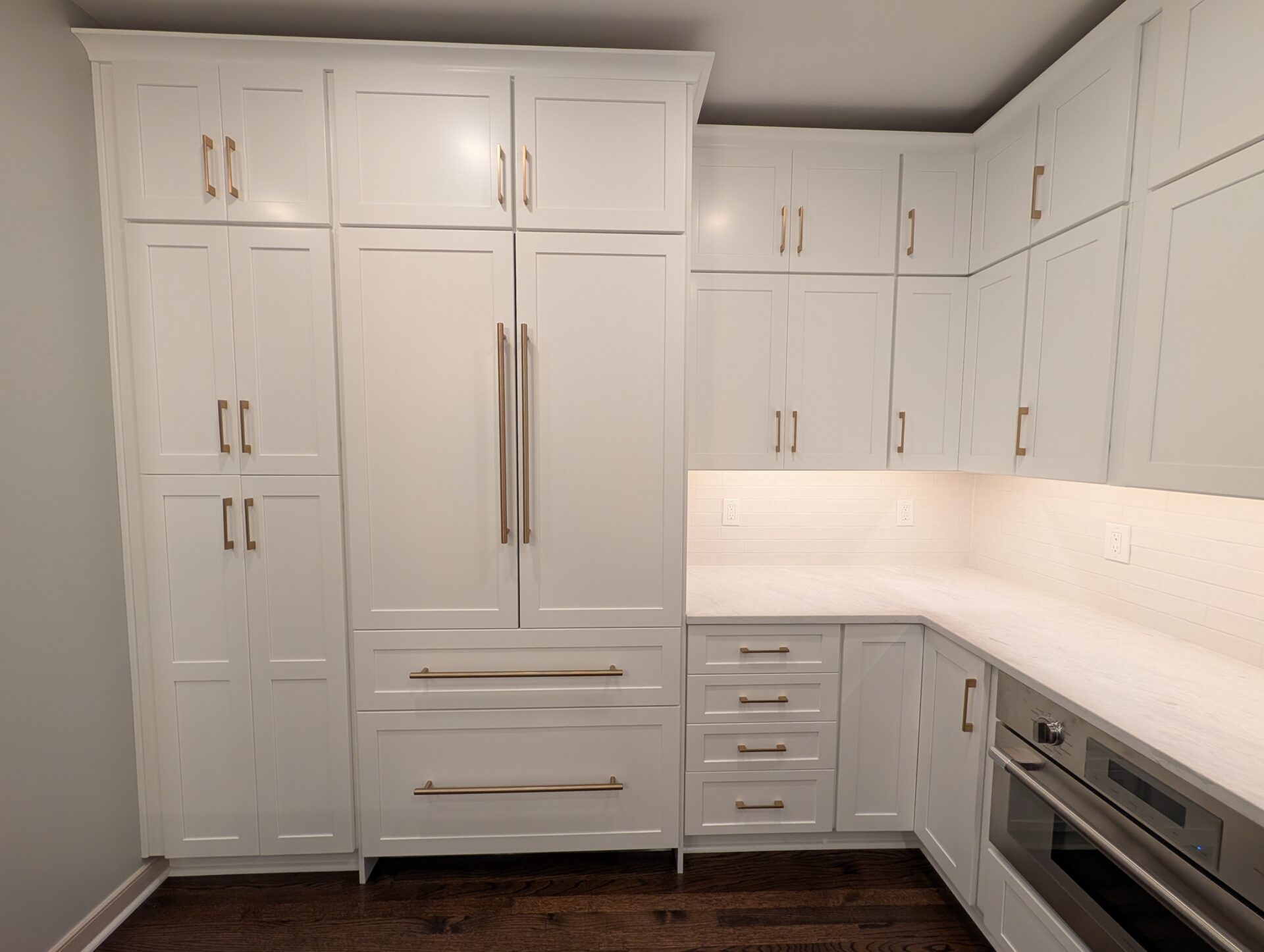 Floor to ceiling white pantry cabinets with brass hardware and panel-ready refrigerator