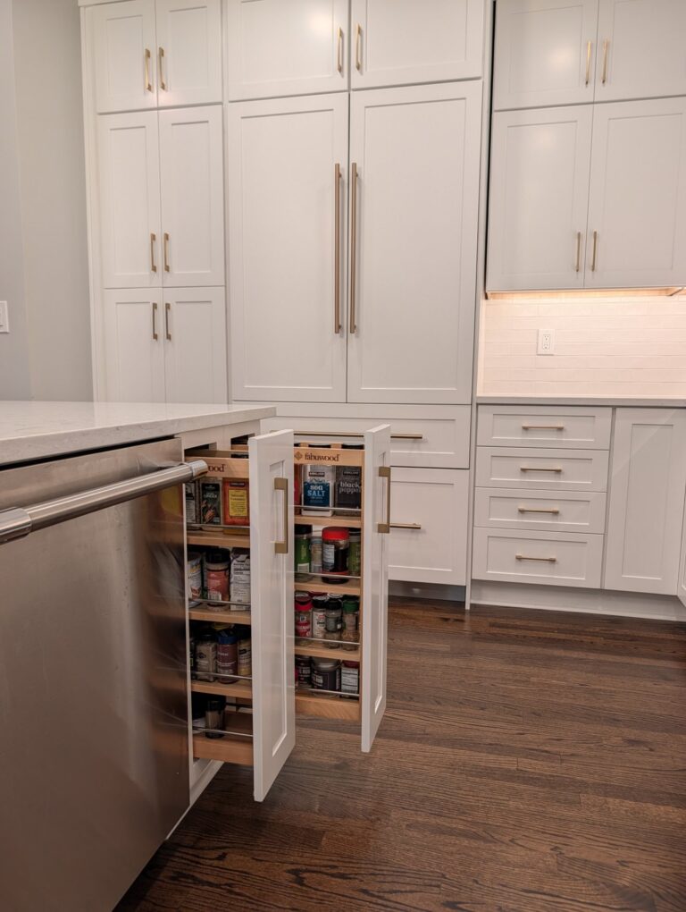 Two Fabuwood pull-out spice racks open beside a dishwasher in the kitchen island