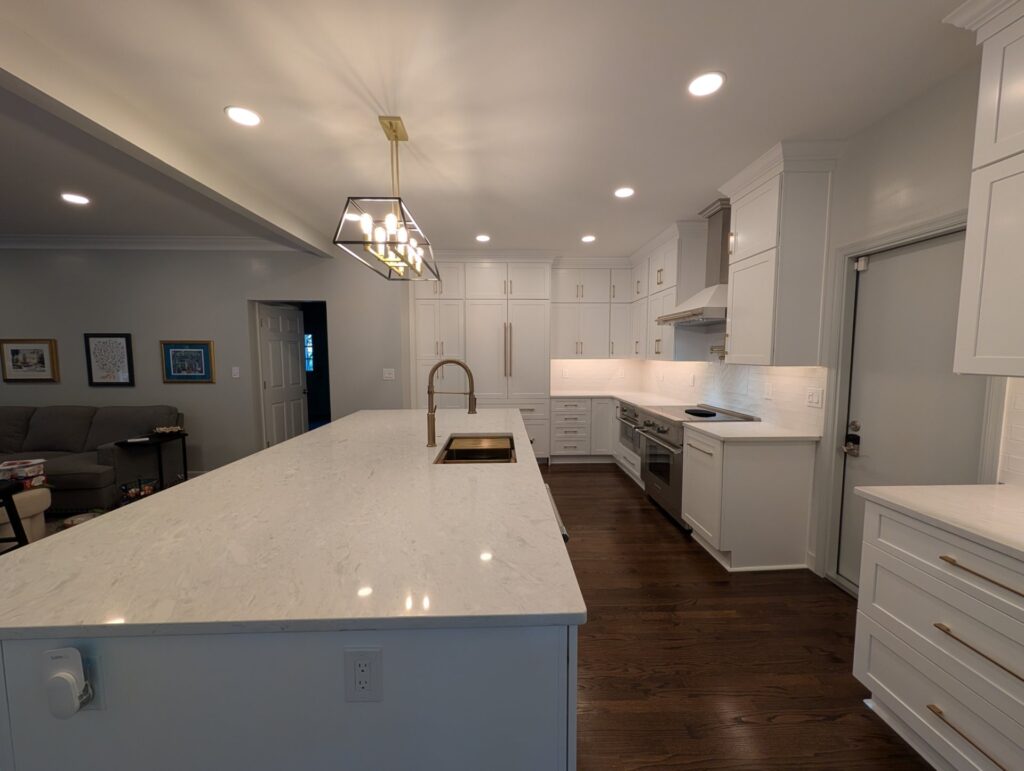 Long quartz-topped kitchen island with gold faucet opening into the living room after the wall was removed
