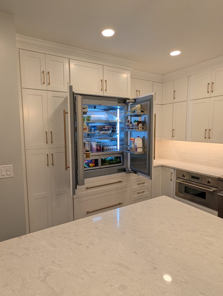 Panel-ready refrigerator open inside a wall of Frost shaker pantry cabinets with crown molding to the ceiling