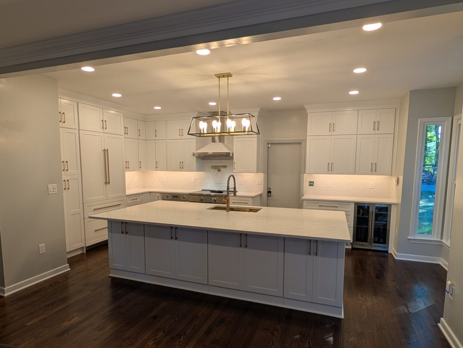 Finished Rockville kitchen remodel with white shaker cabinets to the ceiling, a large island with gold faucet, lantern light and beverage refrigerator
